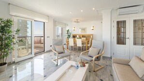 Uma sala de estar moderna com uma porta de vidro que dá para uma varanda, um espaço de jantar com uma mesa e cadeiras de madeira, e um sofá.