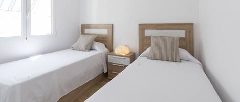 Una habitación con dos camas individuales, una mesita de noche con lámpara y una ventana.