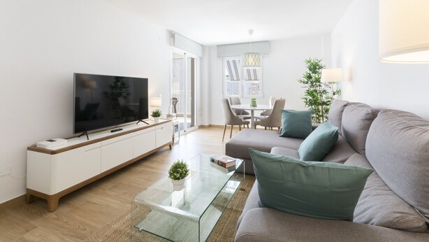 A modern living room with a flat-screen TV, a glass coffee table, a grey sofa with teal cushions, and a dining area with a table and chairs. - VORAMAR II - only families (Playa de Gandía)