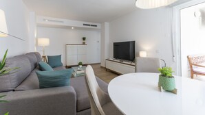 A modern living room with a sofa, a coffee table, a TV, and a dining area. - VORAMAR II - only families (Playa de Gandía)