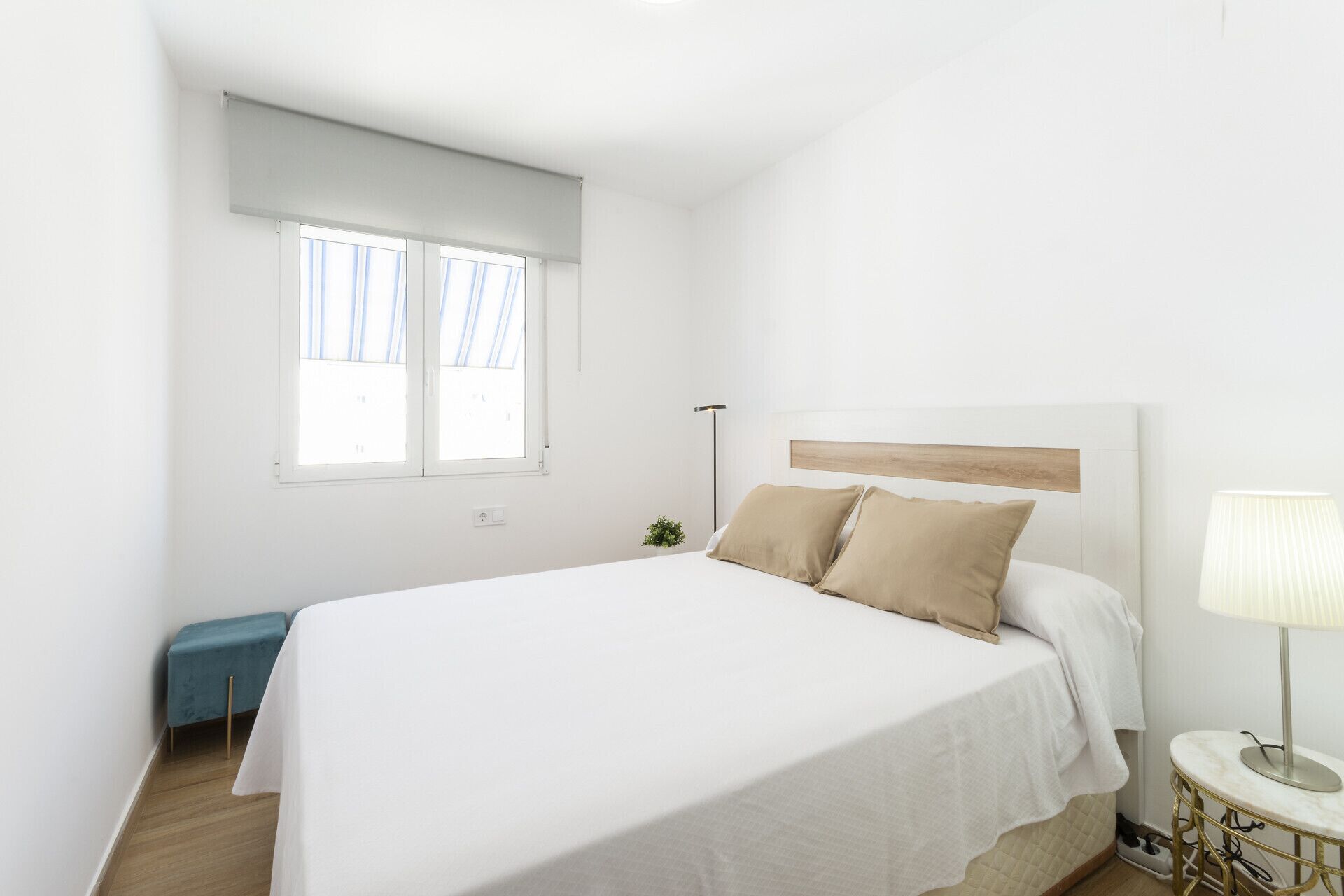 A bedroom with a bed, a bedside table, a lamp, a window, and a small plant.