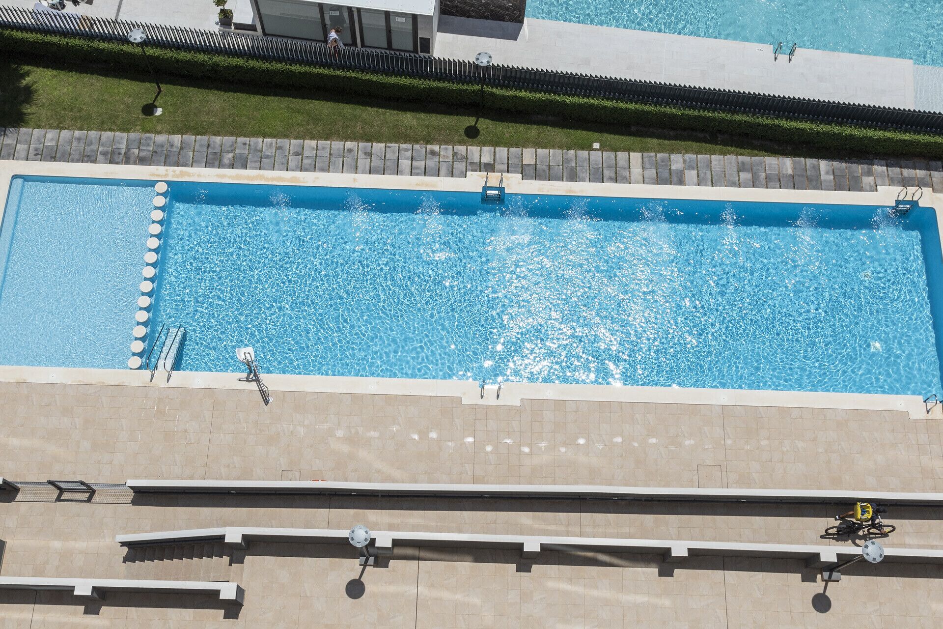 En rektangulär swimmingpool med ett klart, blått vatten och en omgivande poolterrass som är belagd med plattor.