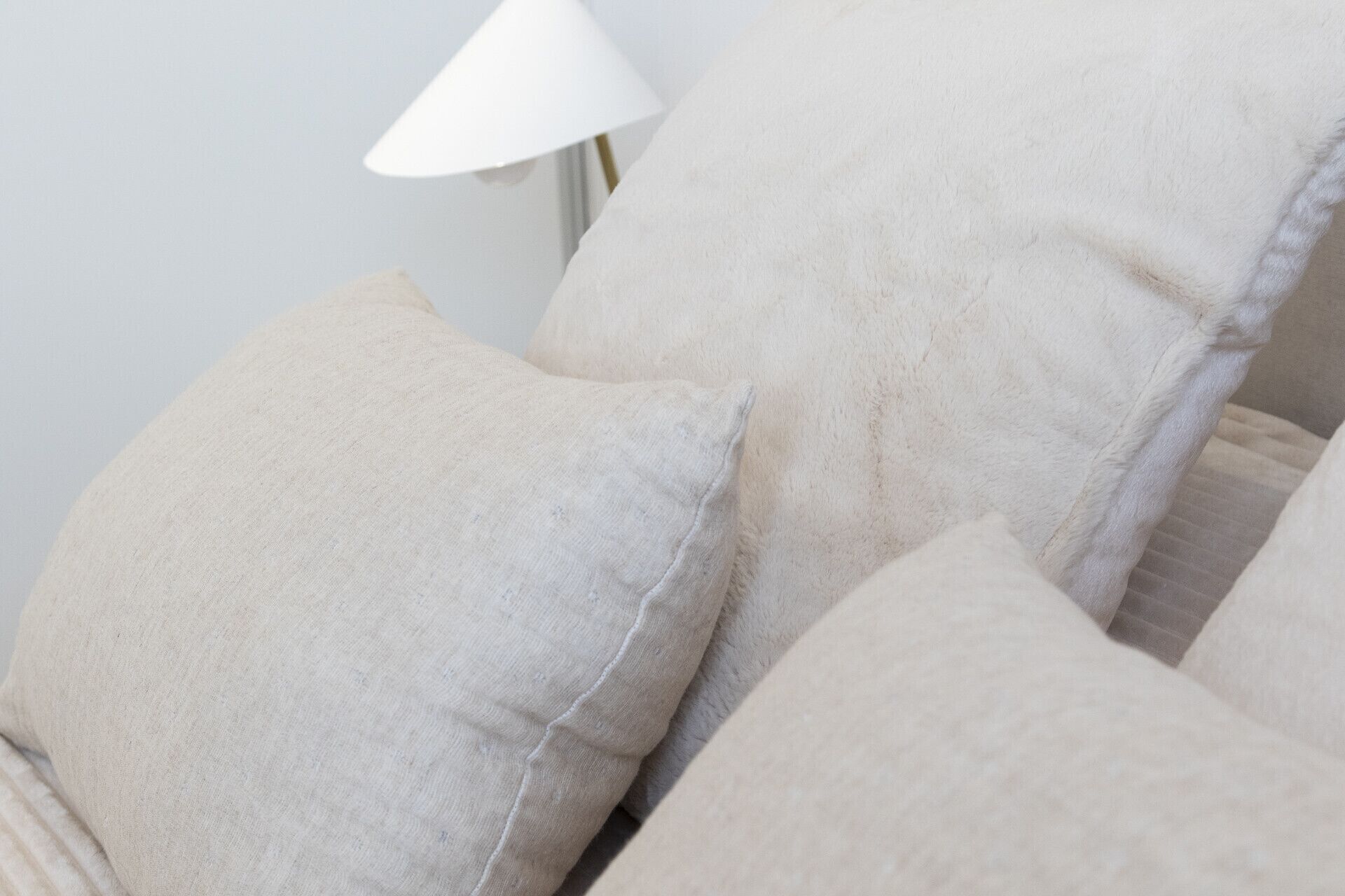 Un gros plan d’un canapé avec des coussins de couleur beige et une lampe blanche en arrière-plan.