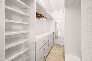 Ein schmaler Gang mit weißen Wänden, Holzboden, einer weißen Kommode mit Schubladen und einem Spiegel an der Wand.