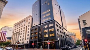 Ein mehrgeschossiges Hotel mit einer gut sichtbaren 'HOTEL'-Beschriftung, einer modernen Glasfassade und einem Straßenbild mit Autos und Ampeln.