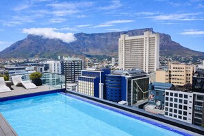 Piscina no terraço com vista para a cidade e montanhas ao fundo.