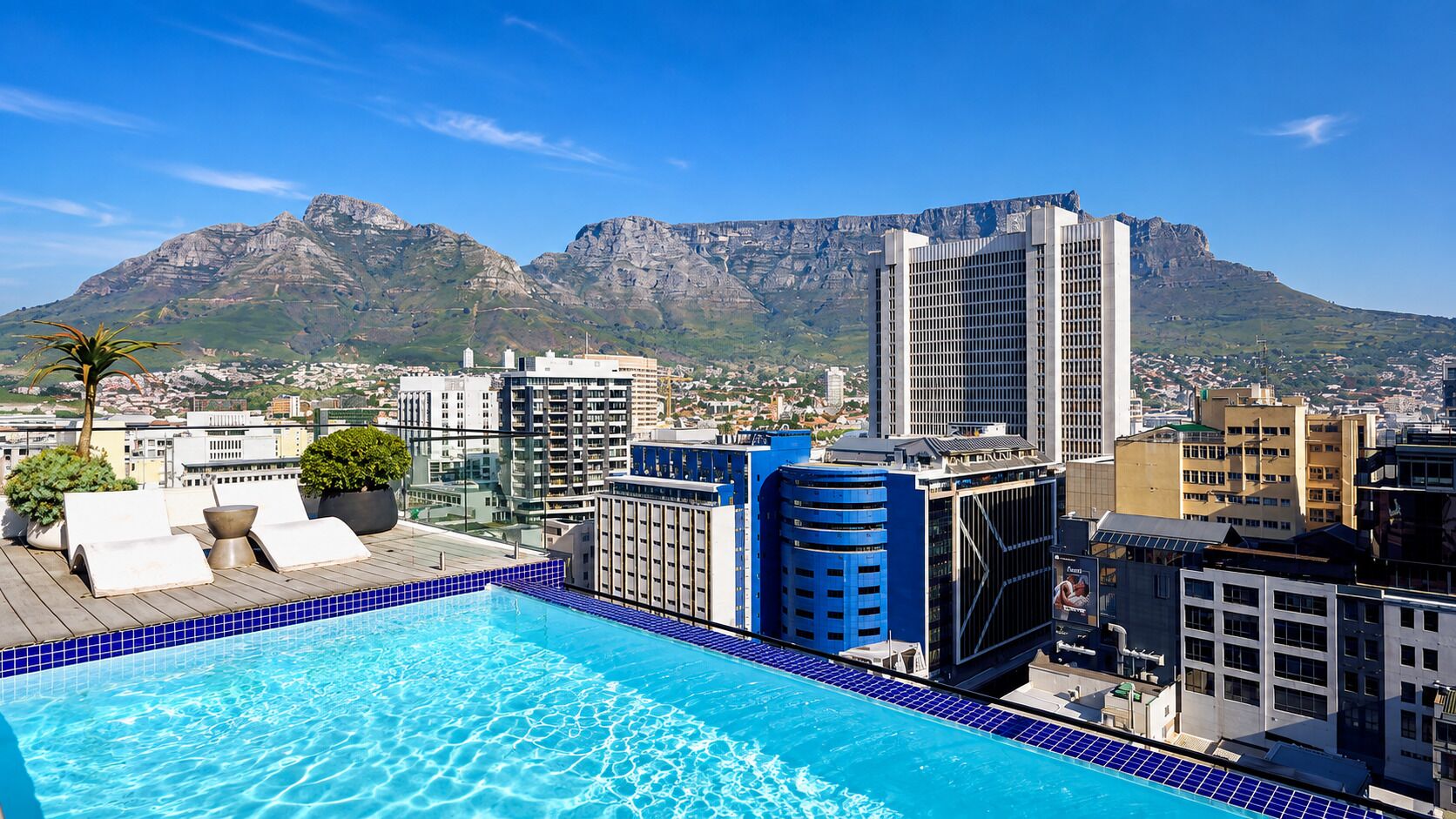 Uma piscina no terraço com vista para a cidade e montanhas ao fundo.
