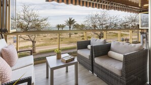 A balcony with wicker furniture, a table, and a view of a beach and trees. - Luxury vacations in Bermuda Apartments in front of the beach - ONLY FAMILIES (Playa de Gandía)