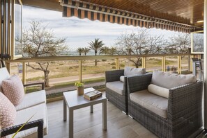 Ein Balkon mit Korbmöbeln, einem Tisch und Blick auf Strand und Bäume.