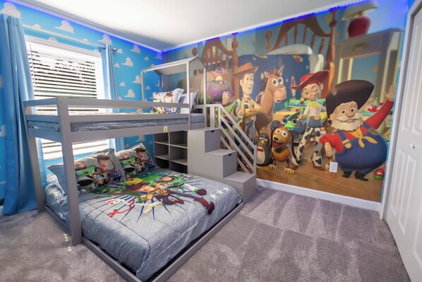 Un lit superposé orné d’une affiche de Buzz l’Éclair et de Woody, une fresque murale représentant les personnages de Toy Story, et une fenêtre avec des stores.