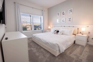 Une chambre à coucher comprenant un lit, des tables de chevet, une commode, une fenêtre avec des stores et des œuvres d’art murales.