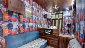 Zona de recepción de hotel con un mostrador de madera, un sofá azul y una pared con diseño.