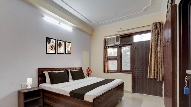 Un dormitorio con cama de madera, mesita de noche, decoración en la pared y una ventana con cortinas.