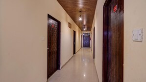 Un pasillo largo y estrecho con puertas de madera a ambos lados, suelo de baldosas y techo de madera.