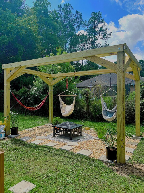 A wooden pergola with two hammocks, a table, and potted plants in a garden setting.