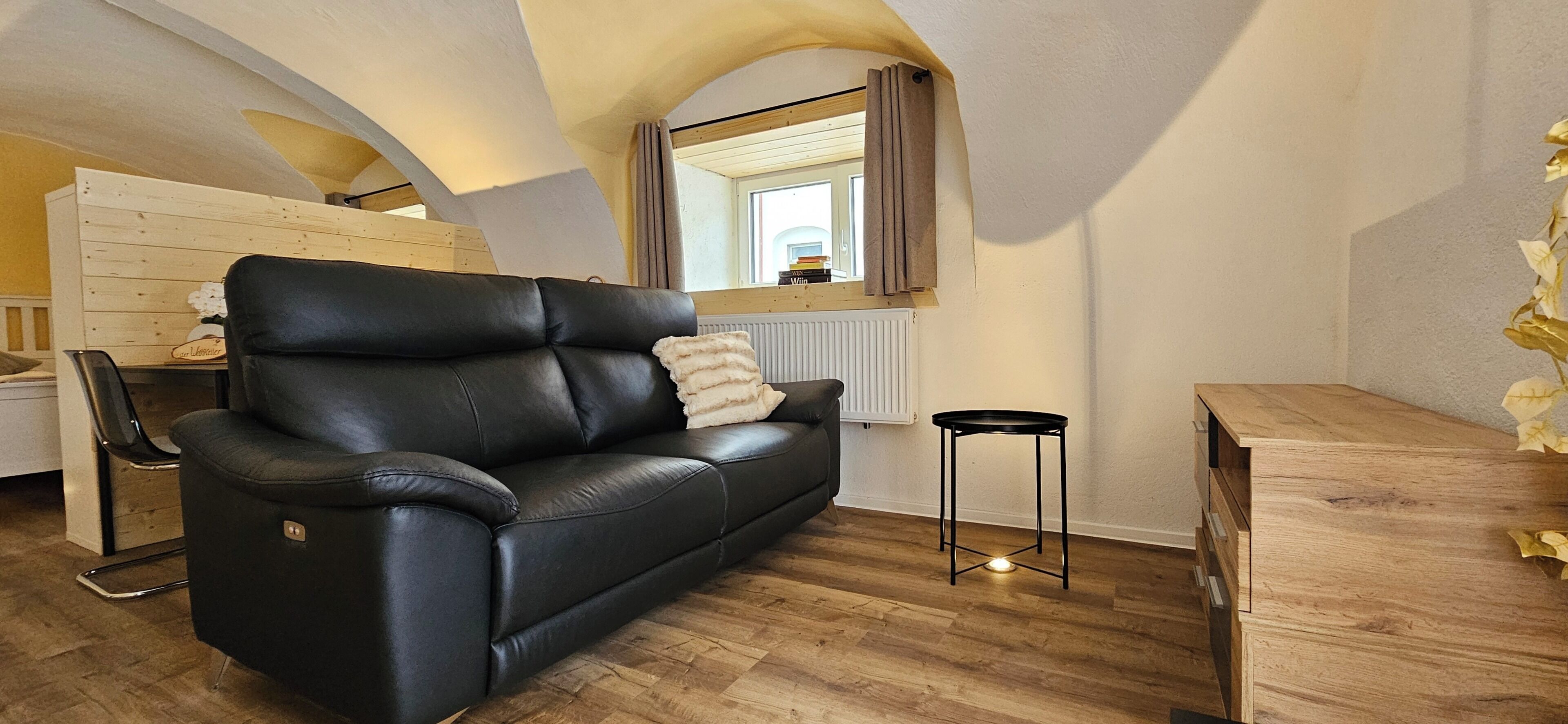 Ein modernes Wohnzimmer mit einem schwarzen Ledersofa, einem Holztisch und einer Holzkommode.