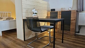 A compact room with a bed, a small table, a chair, and a radiator.