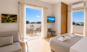 Ett hotellrum med en balkong, en säng, en soffa, ett litet bord och en TV.