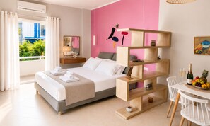 Ein modernes Schlafzimmer mit Bett, Nachttischen, einer Holzregaleinheit, einer Essecke mit Tisch und Stühlen sowie Blick auf Grünfläche.