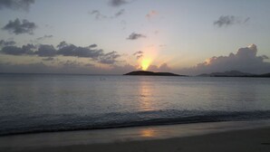 En strand med roligt vand, solnedgang og fjerne landskaber.