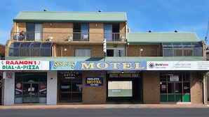 A building with a sign for 'SISLEY'S MOTEL' and a 'RAAMON'S DIAL-A-PIZZA' across the street. - Sisleys Motel (Lismore)