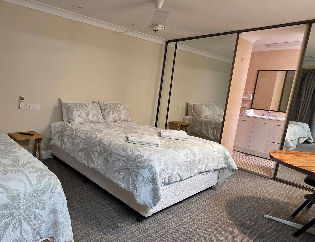 A hotel room with a large bed, a small table, a mirror, and a bathroom visible through an open door.