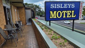 A motel sign, outdoor seating, and a road with vehicles. - Sisleys Motel (Lismore)