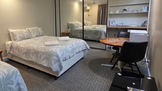 A hotel room with a bed, a desk, a chair, a mirror, and a kitchenette. - Sisleys Motel (Lismore)
