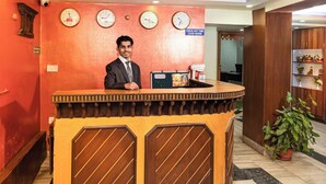 A reception desk with clocks, a sign indicating check-out time, and a potted plant. - Hotel Holiday Regency  (Kathmandu)