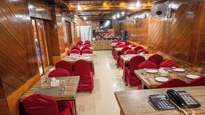 A long dining hall with rows of tables and chairs, wooden walls, and ceiling fans. - Hotel Holiday Regency  (Kathmandu)
