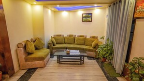 A living room with a sofa, a coffee table, and a painting on the wall. - Hotel Holiday Regency  (Kathmandu)