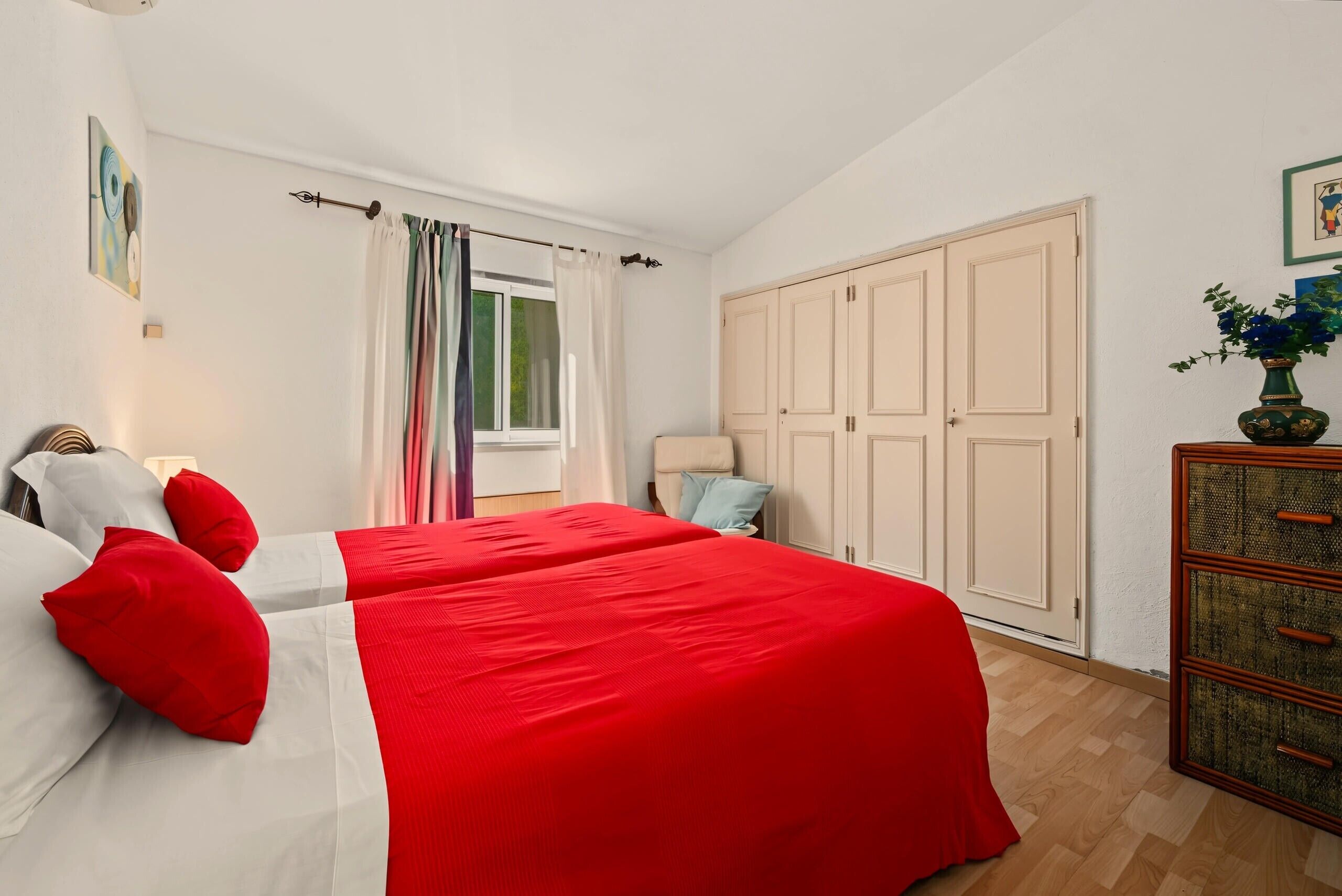 Ein Schlafzimmer mit zwei Betten, einem Kleiderschrank, einem Fenster mit Vorhängen und einer Pflanze auf einem Schrank.