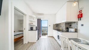 A compact kitchen with a washing machine, a dining area with a table and chairs, and a view through a door. - Holiday Home 'Belavista - By Staywise' with Sea View, Wi-Fi and Air Conditioning (Portimão)
