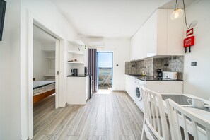 Eine kleine Küche mit Waschmaschine, ein Essbereich mit Tisch und Stühlen sowie ein Blick durch eine Tür.