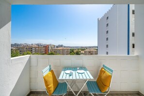 A balcony with a table and chairs, a clear view of the cityscape, and a building with a blue stripe. - Holiday Home 'Belavista - By Staywise' with Sea View, Wi-Fi and Air Conditioning (Portimão)
