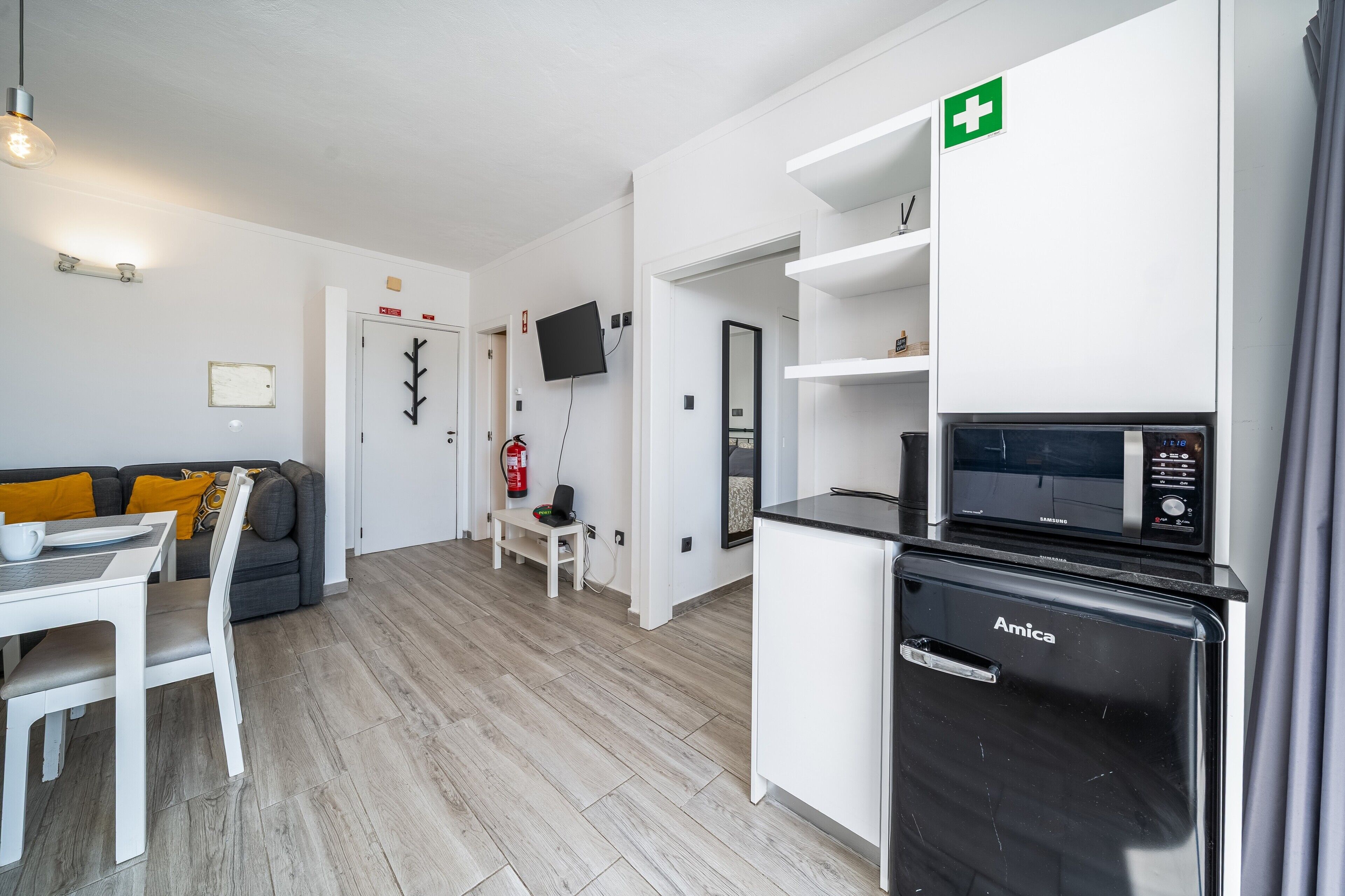 A modern kitchen with a microwave, an Amica refrigerator, and a flat-screen TV mounted on the wall.