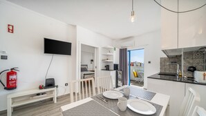 A modern kitchen with a flat-screen TV, a dining table with plates and cutlery, a bench, and a fire extinguisher. - Holiday Home 'Belavista - By Staywise' with Sea View, Wi-Fi and Air Conditioning (Portimão)