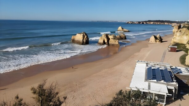 A beach with large rock formations, a sandy shore, and a building with solar panels. - Holiday Home 'Belavista - By Staywise' with Sea View, Wi-Fi and Air Conditioning (Portimão)