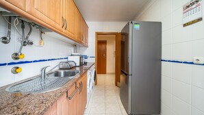 Een keuken met houten kastjes, een roestvrijstalen spoelbak, een wasmachine en een koelkast.