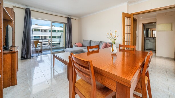 Een ruime eethoek met een houten tafel en stoelen, een bank en uitzicht op een gebouw door grote ramen.