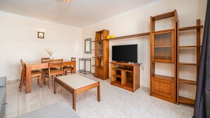 Een woonkamer met een eettafel, stoelen, een televisie, houten planken en een bank.