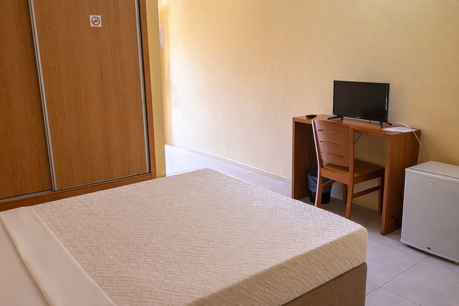 A bedroom with a bed, a desk with a computer, and a small refrigerator.