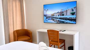 Una habitación de hotel con una cama, un escritorio, una silla y un cuadro de una calle nevada.