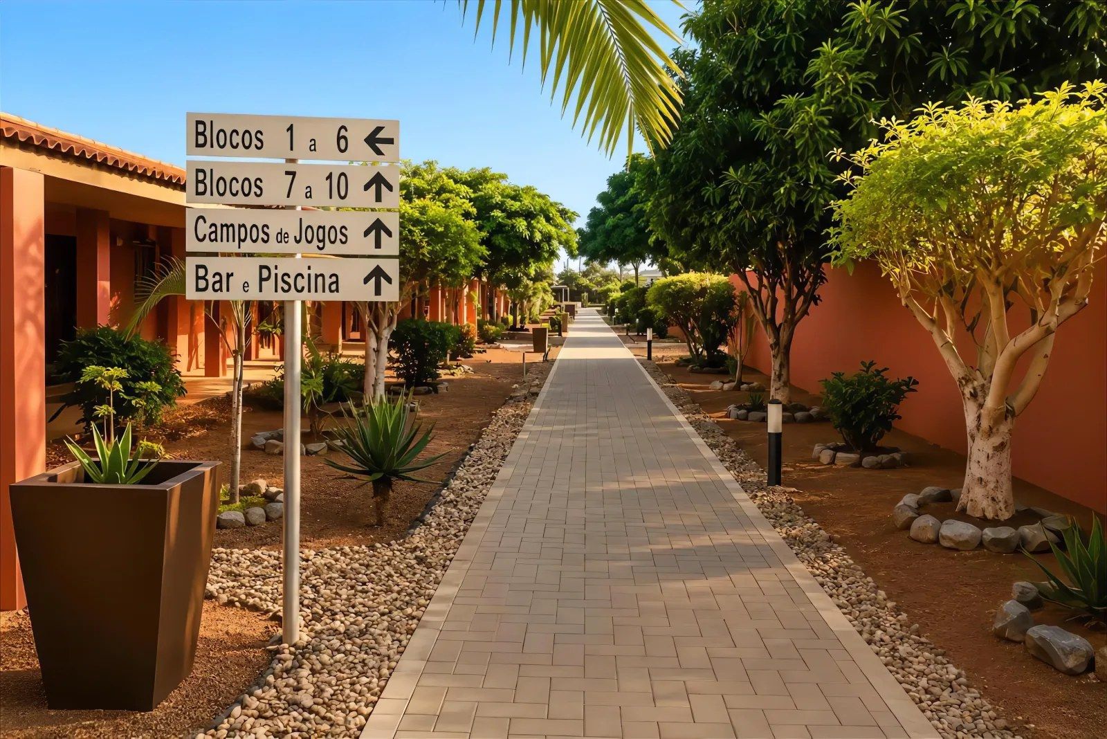 A pathway lined with palm trees and potted plants, leading to a building with a sign indicating directions to various amenities.