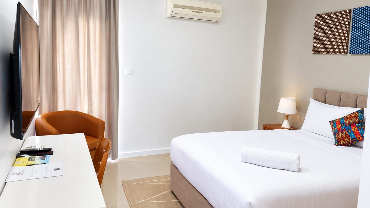 Habitación de hotel con cama, escritorio con silla, televisor y aire acondicionado instalado en la pared.