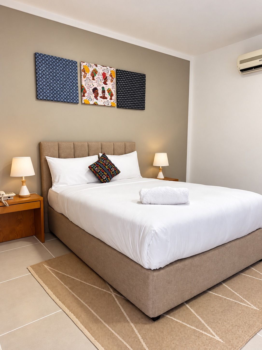 A hotel room with a large bed, two bedside tables with lamps, and three wall art pieces.