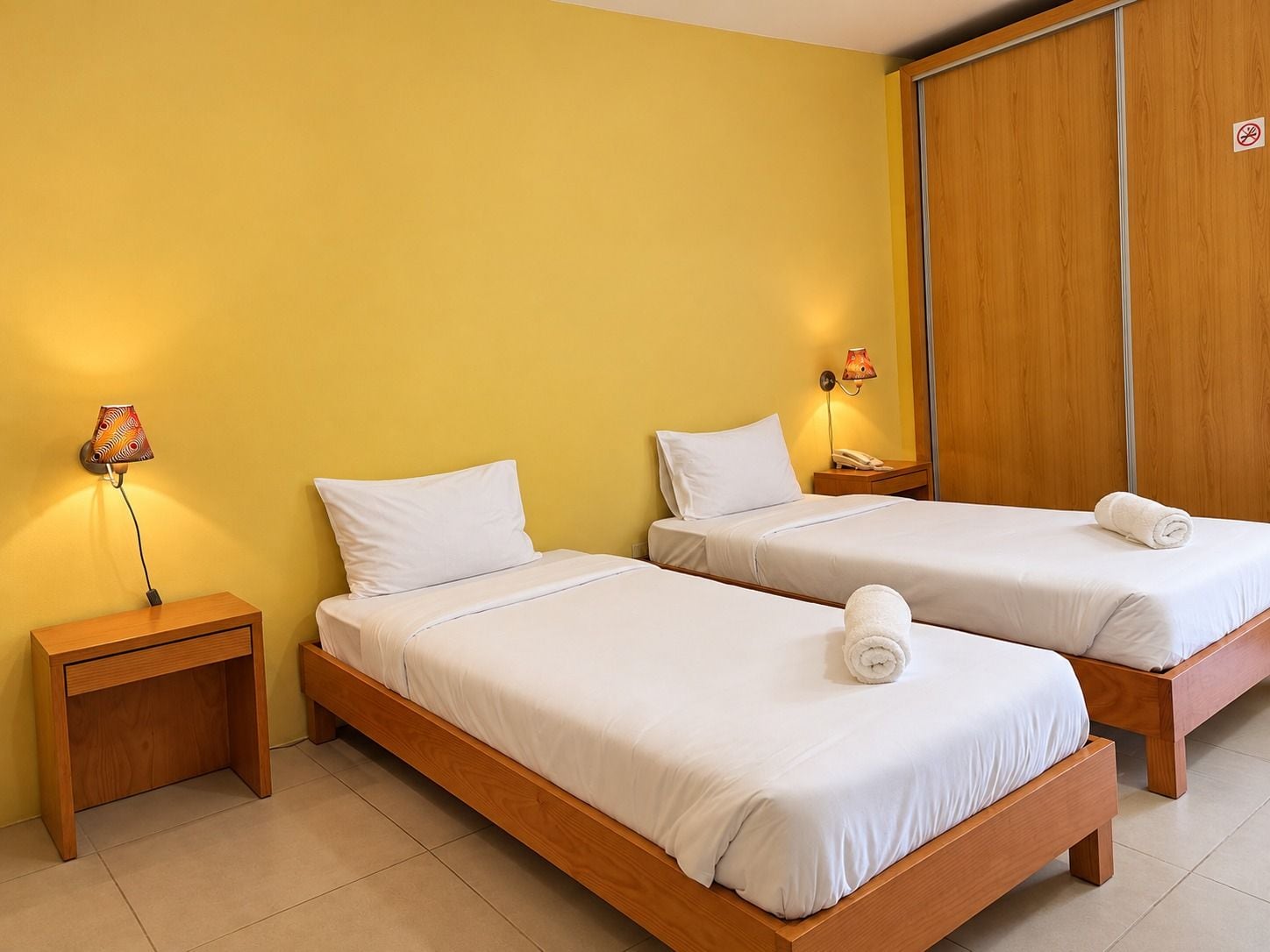 A hotel room with two beds, a nightstand, a lamp, and a wooden wardrobe.