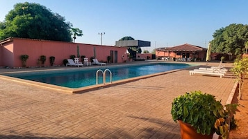 Una piscina con sillones de descanso, una zona cubierta y un patio de ladrillo.
