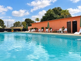 A swimming pool with lounge chairs and umbrellas, surrounded by a building with doors and windows.