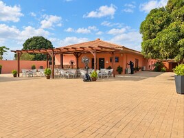 An outdoor patio area with tables and chairs, a covered seating area, and a building with a tiled roof.